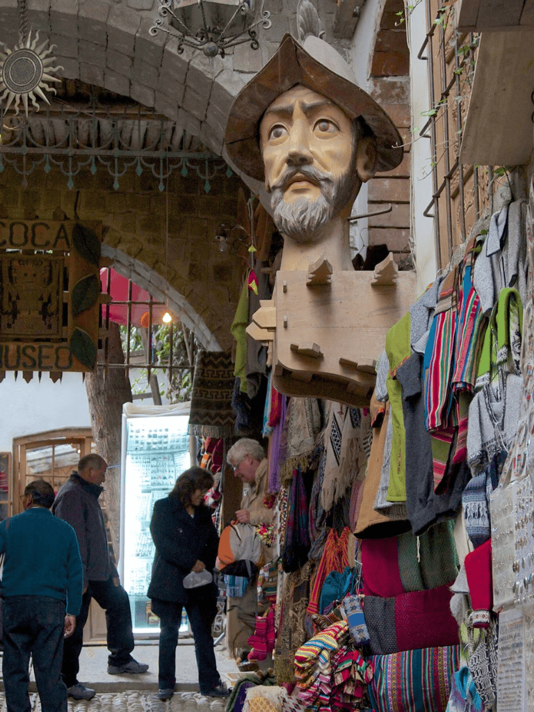 Colorful Mercado street stall with traditional textiles and a large hat-wearing sculpture, vibrant shopping scene, popular tourist destination.