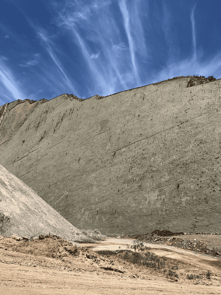 Crane facing a steep construction site, dusty environment with clear blue sky overhead.