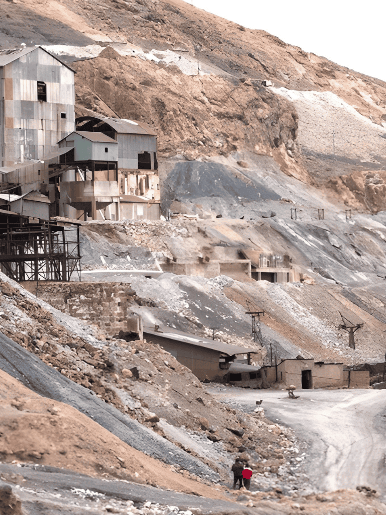 Abandoned mine shaft in a rugged, mountainous landscape with dilapidated structures and uneven terrain.