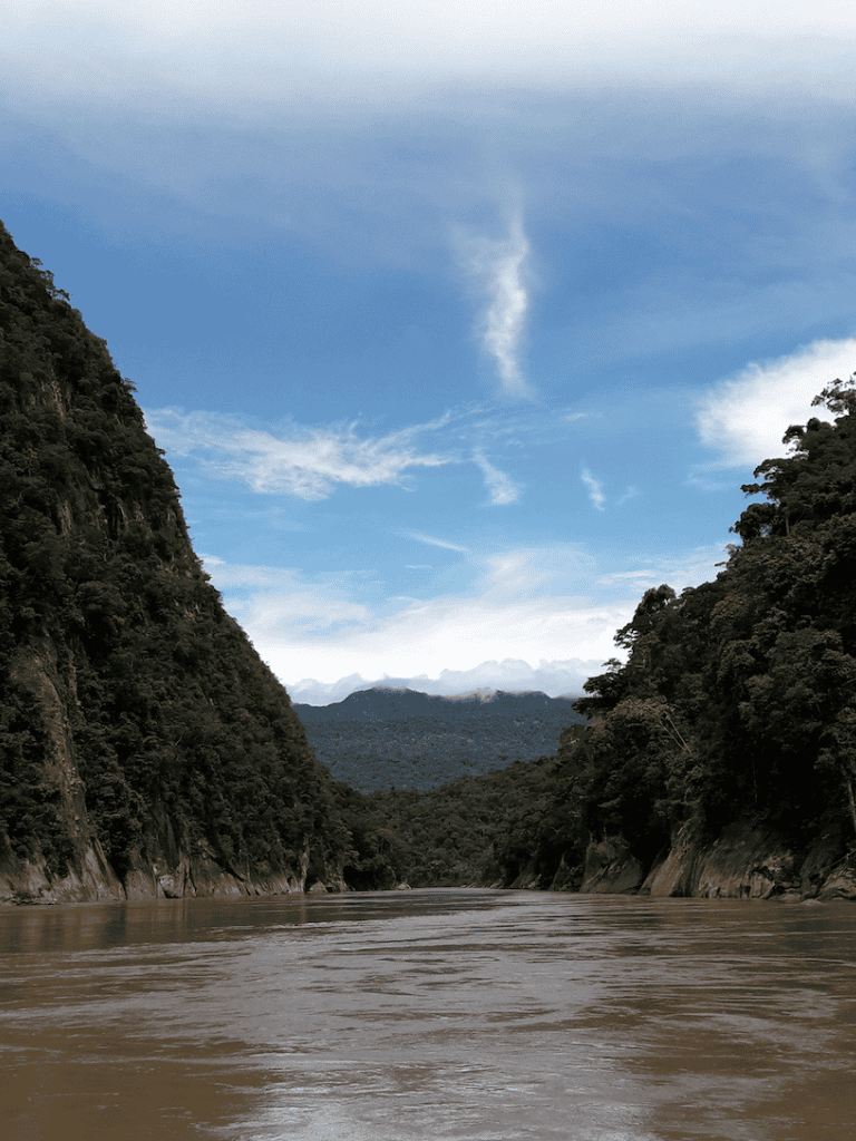Freshwater river flowing through lush green canyon with mountain peaks in the distance, scenic outdoor landscape, QuestForDirections.