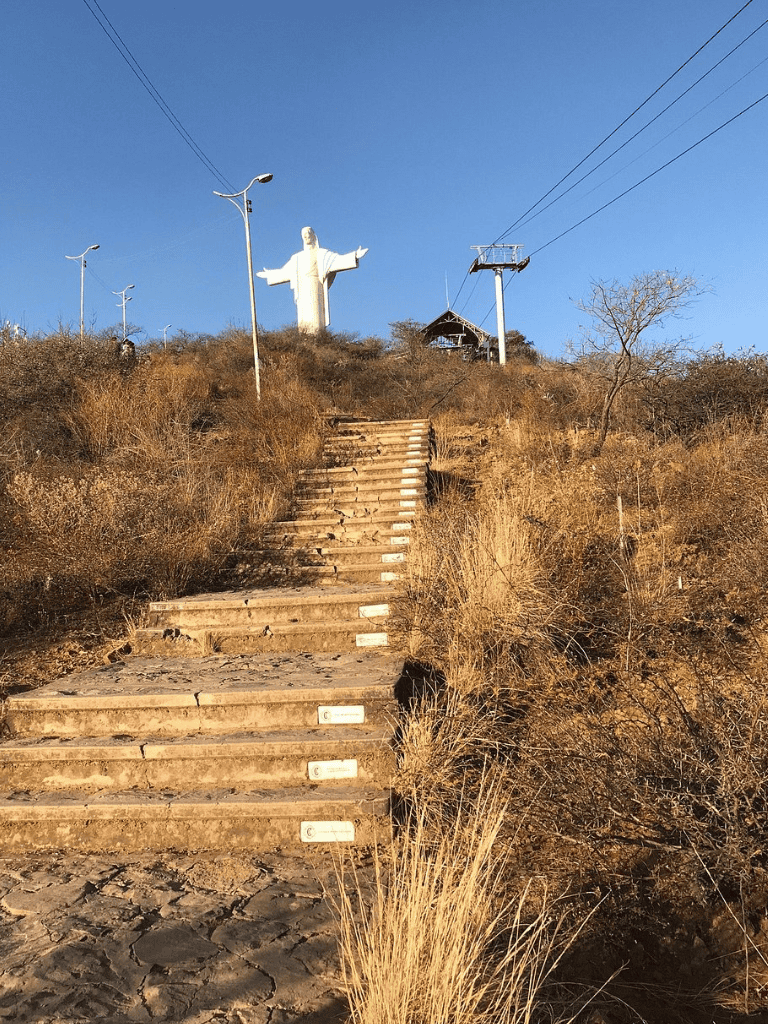 Jesus Christ statue on hill with stairs and dry landscape, ladder of steps leading up to religious monument.