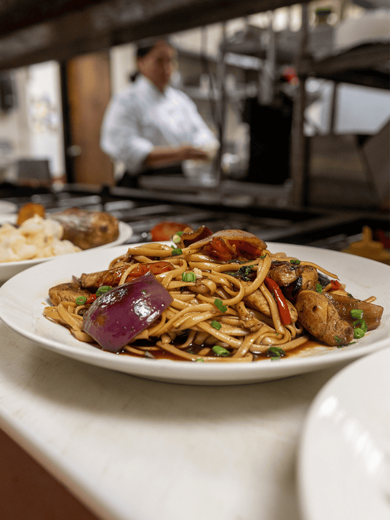 Szechuan stir-fried noodles with vegetables and chicken, served in a restaurant kitchen.