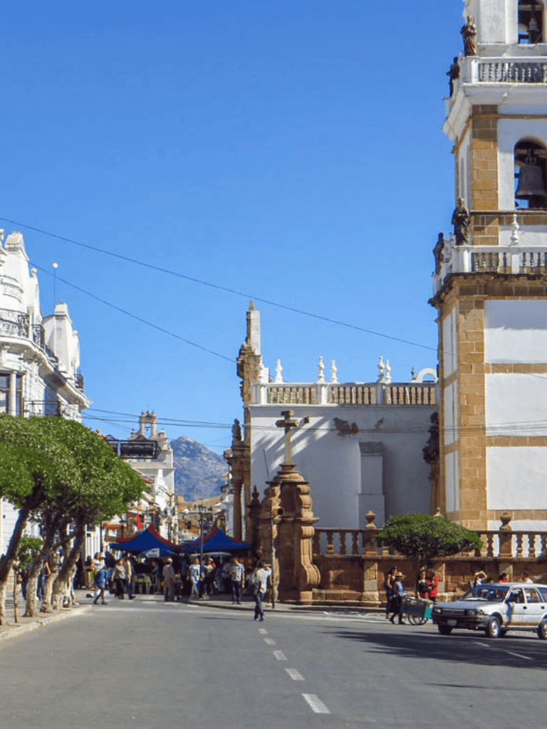 Colorful town square with historic architecture, bustling market, and mountain backdrop in Bolivia.