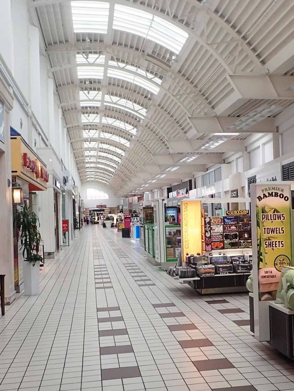 Bright indoor shopping mall with high arched skylights and various retail stores and kiosks.