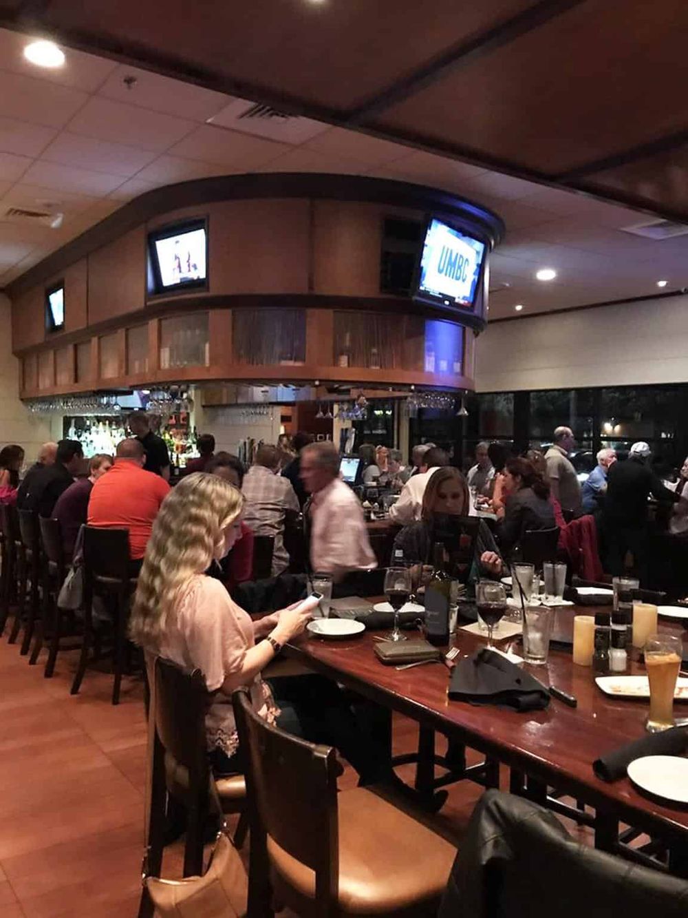 Cozy bar and restaurant scene with patrons enjoying drinks and conversation at a U-shaped bar, upscale ambiance, and dim lighting.