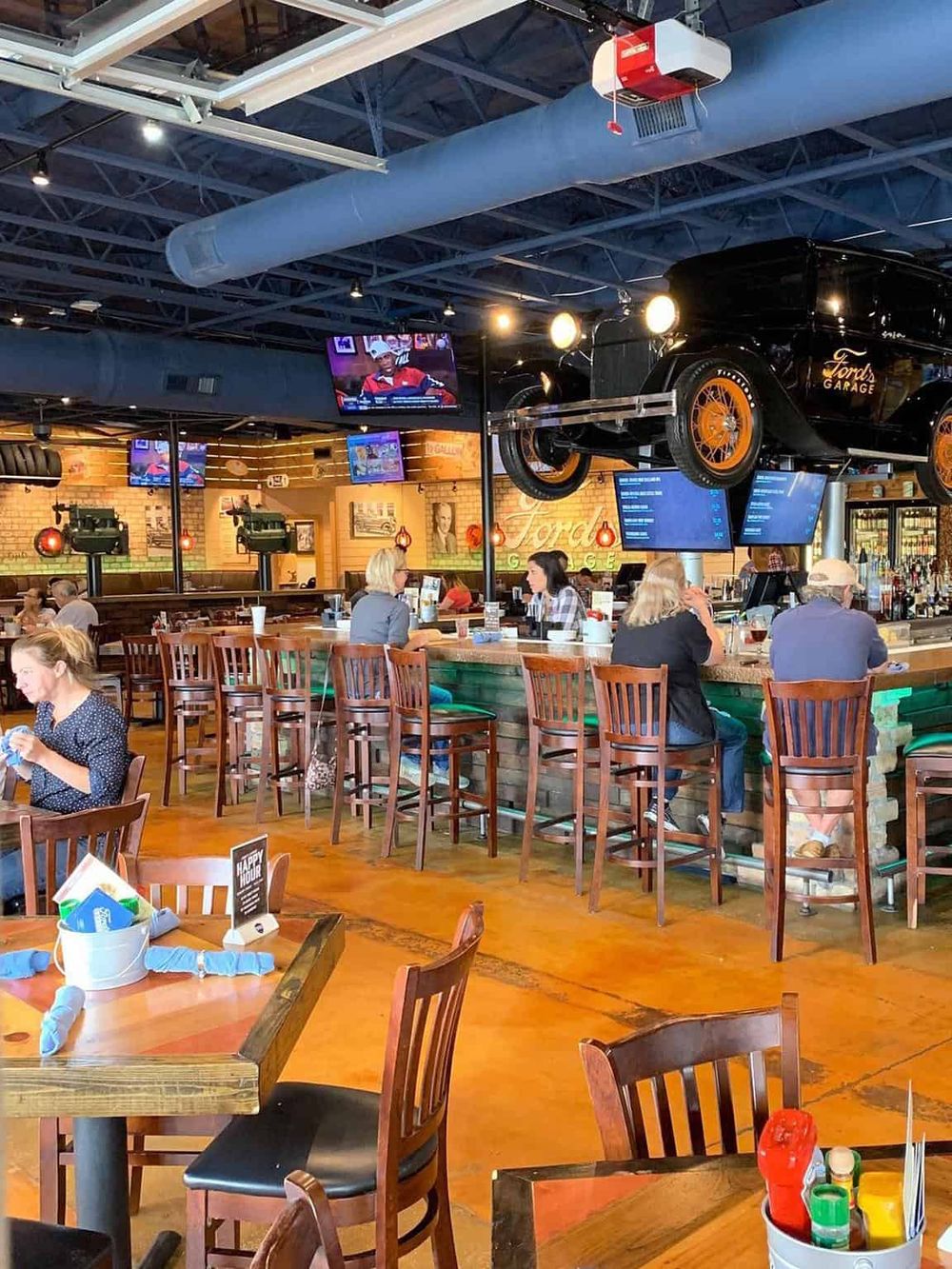 Vibrant bar and restaurant interior with vintage car decor, multiple TV screens, and patrons enjoying their meals.