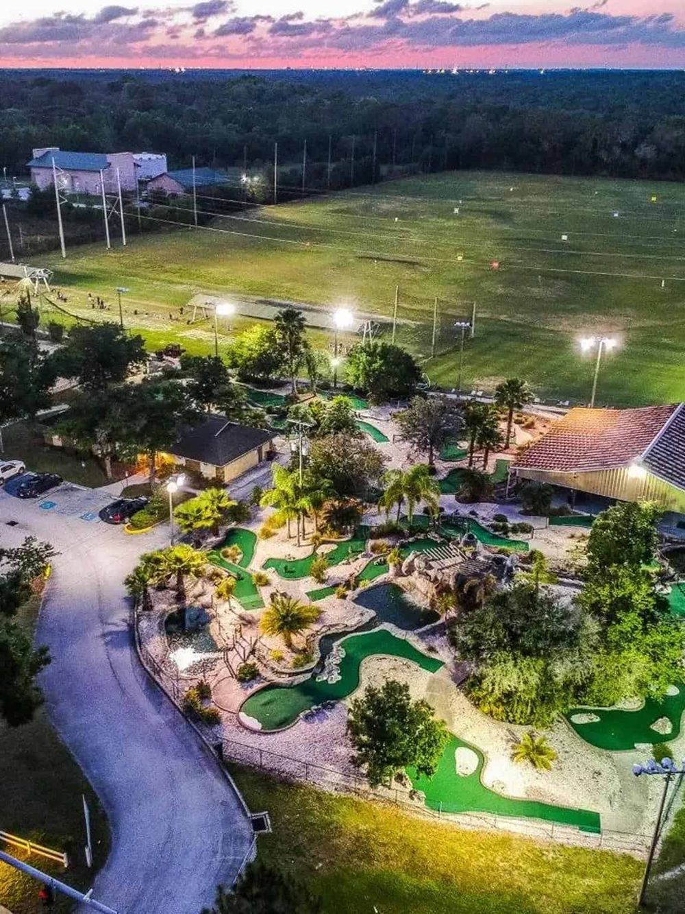 Miniature golf course with lush landscaping and bright lighting at dusk.