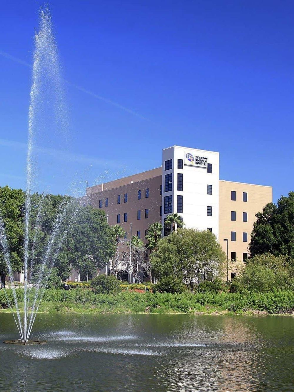 Modern hospital building with fountain and pond, surrounded by greenery in Orlando, Florida.