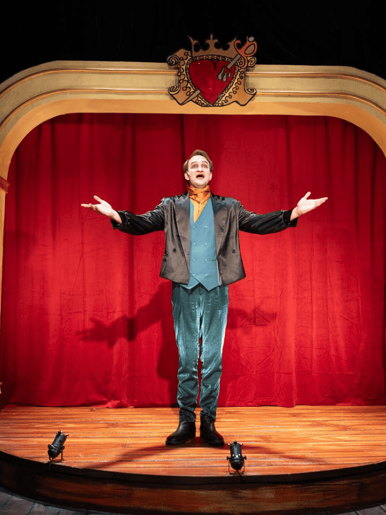 Clown performing on stage with red curtain at QuestForDirections theater.