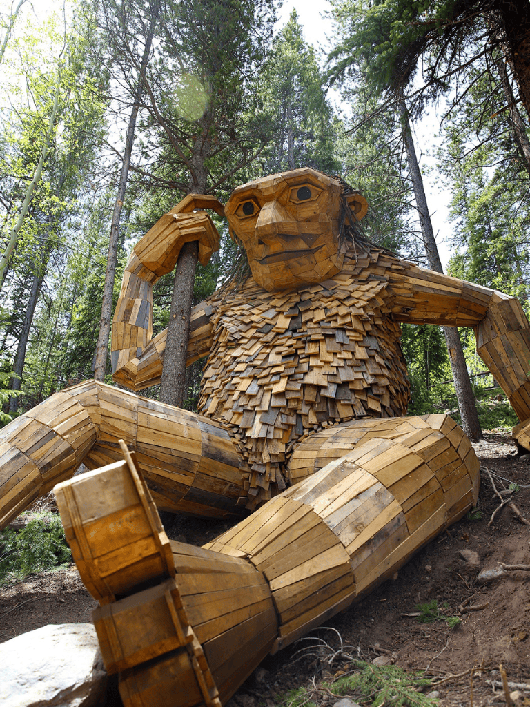 Large wooden monkey sculpture in forest, wildlife art installation for outdoor tourism.