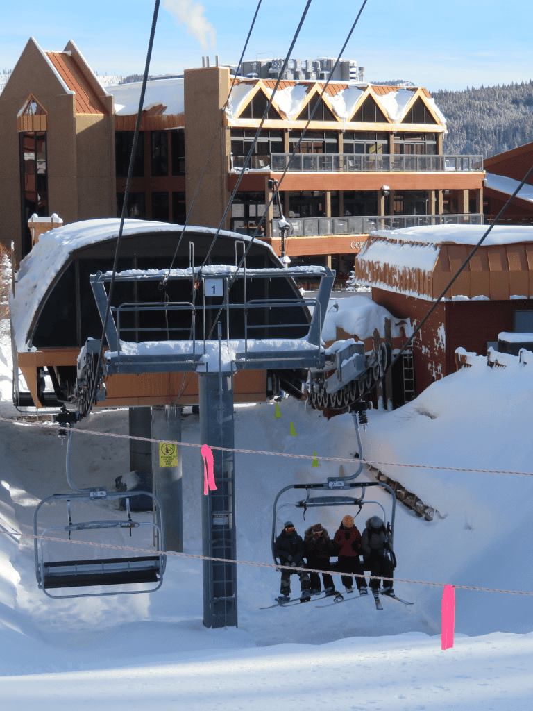 High alpine ski lift and lodge at winter mountain resort with snow-covered slopes and skiers enjoying a day on the mountain.