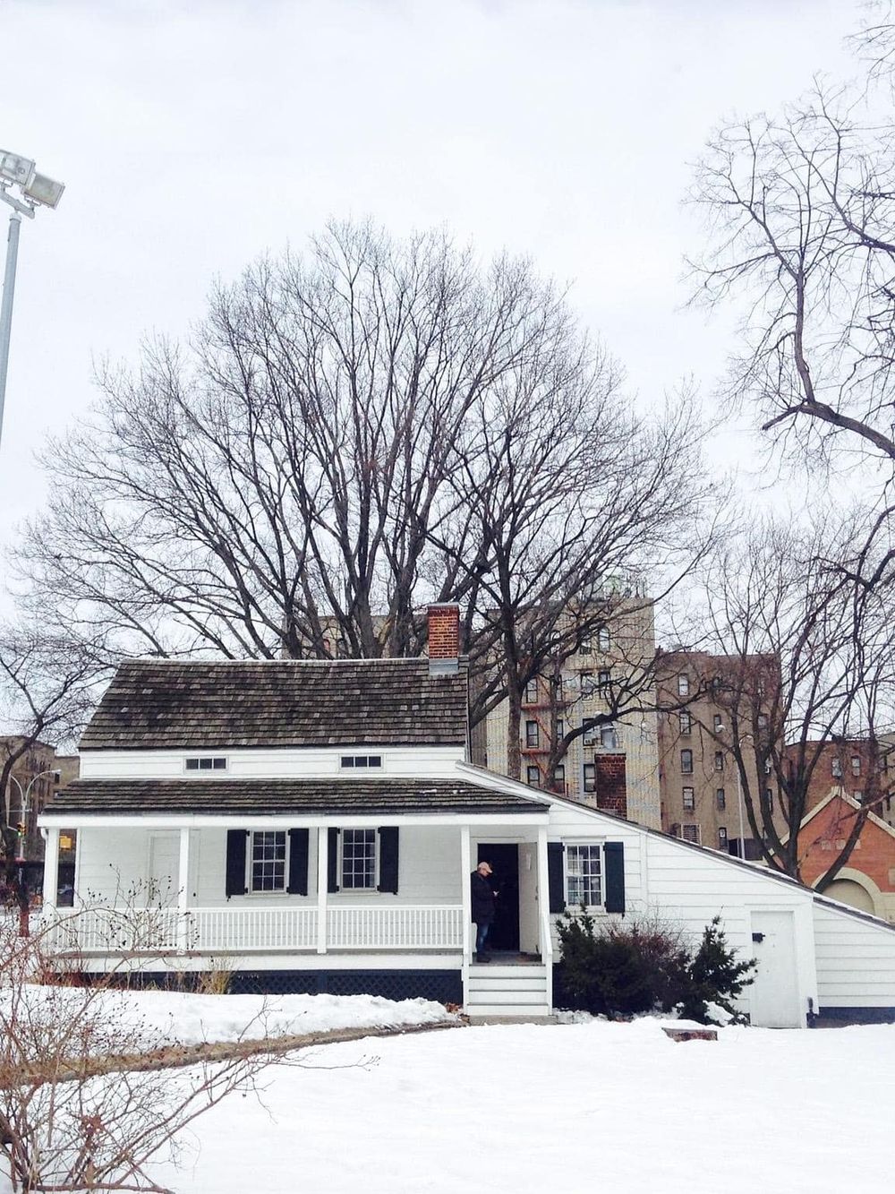 Charming white cottage with black shutters amid snowy landscape, classic example of cozy winter neighborhood scenery.