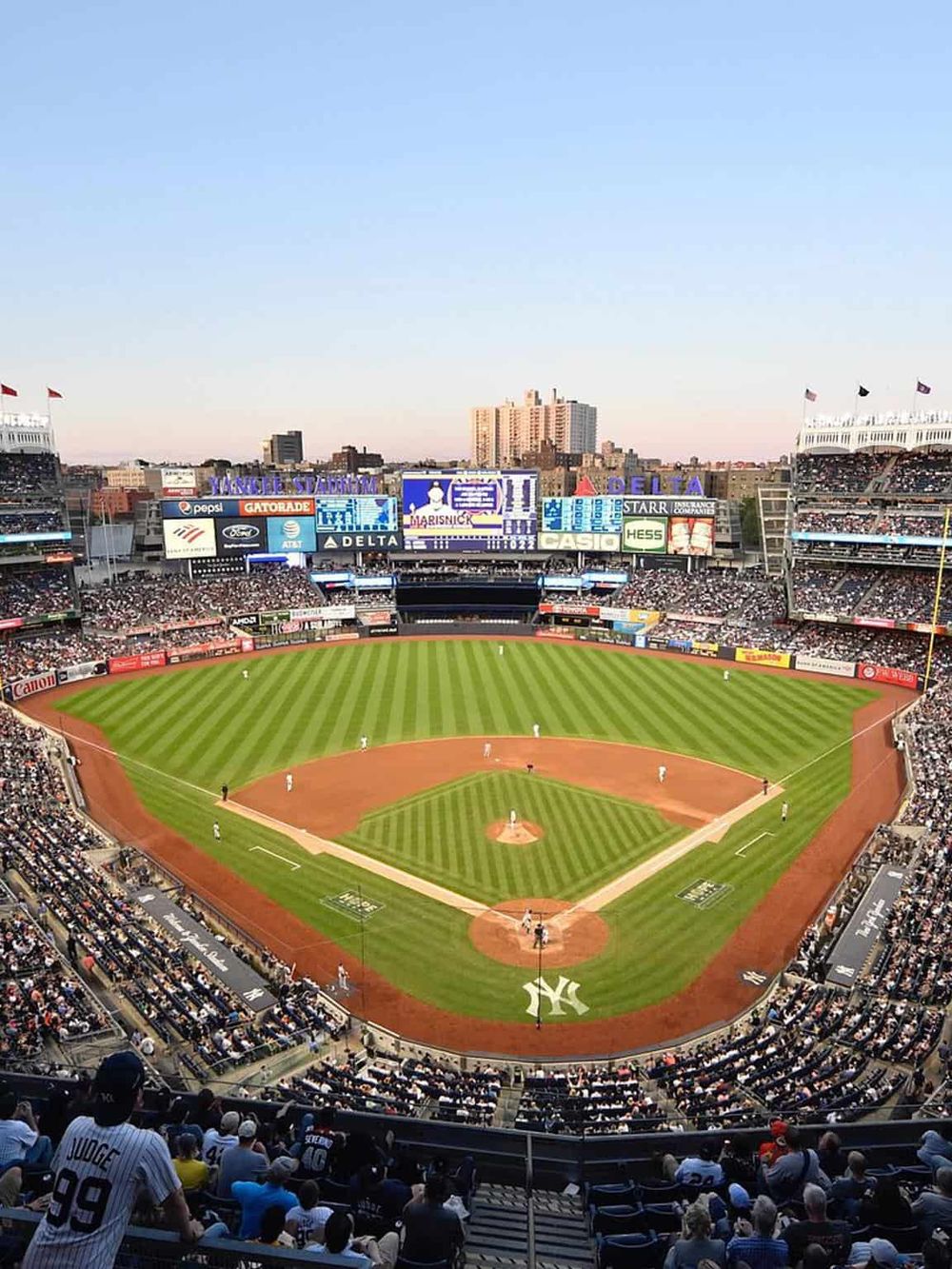 Luxury baseball stadium with New York Yankees infield, packed crowd, and city skyline in the background.
