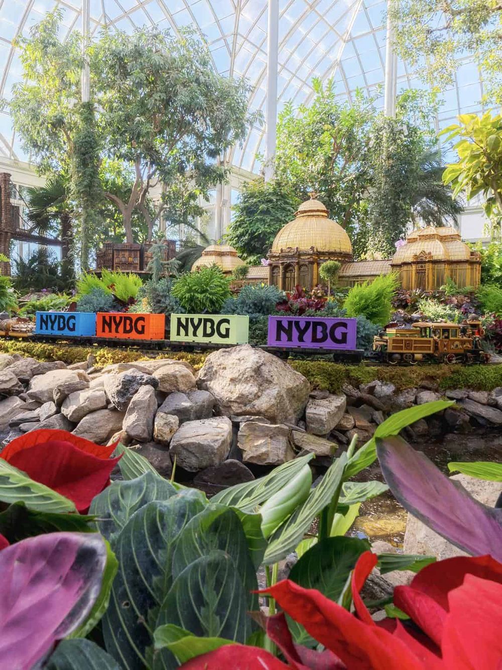 Vibrant botanical display in an indoor conservatory, featuring miniature architectural models and colorful NYBG train cars for botanical exploration.