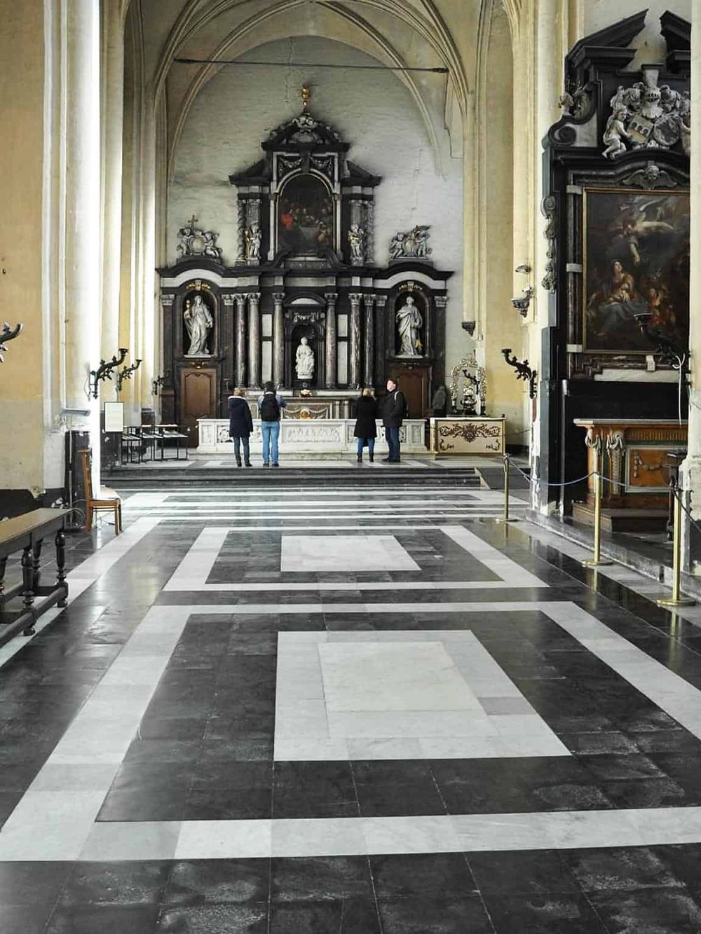 Serene church interior with ornate altar, religious statues, and elegant black-and-white patterned flooring.