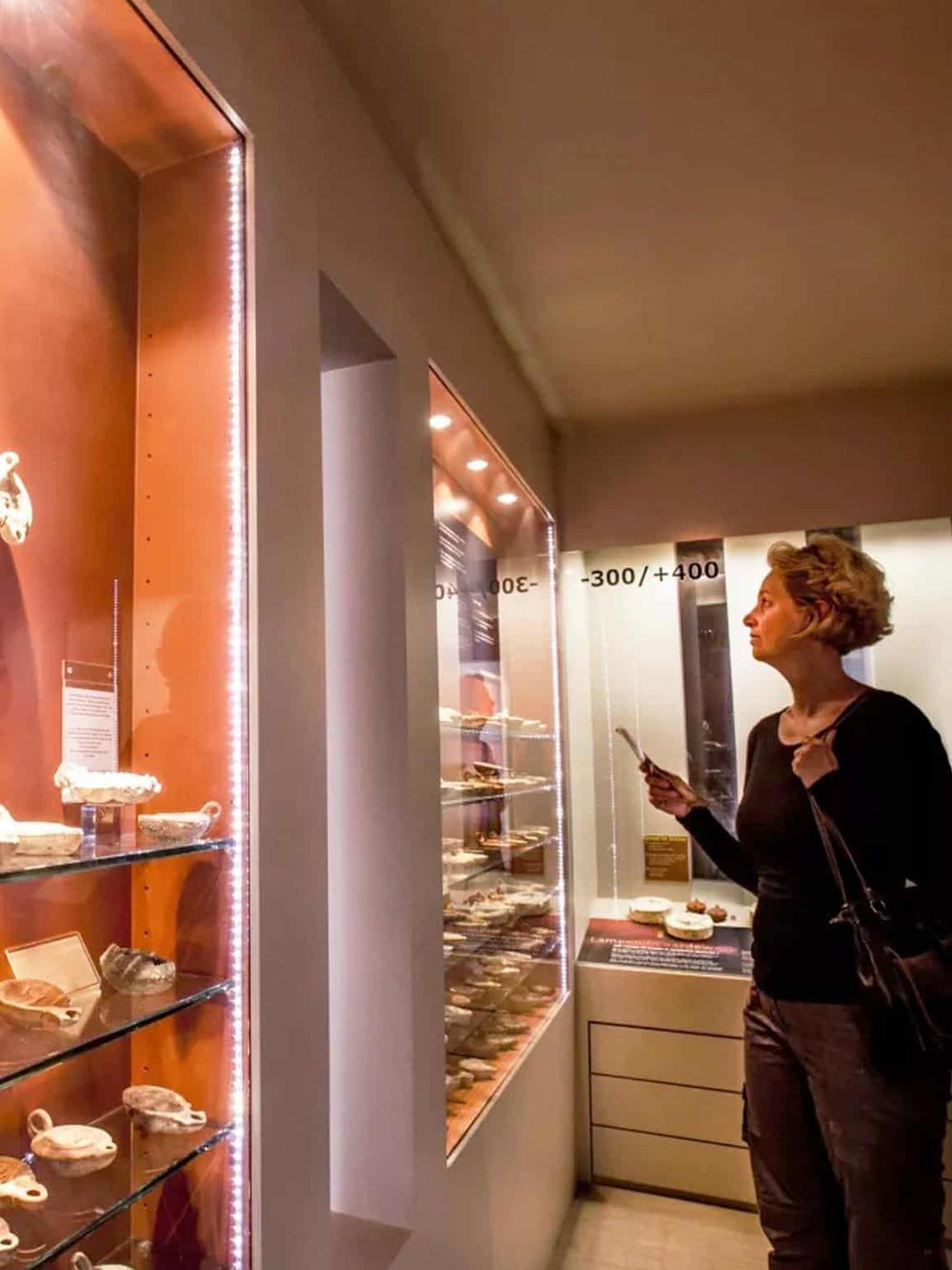Colorful museum display case with shells and artifacts, woman viewing exhibits, educational cultural experience.
