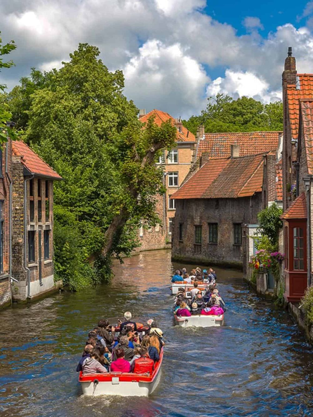 Historic canal tour with sightseeing boats passing charming old European houses in Bruges.