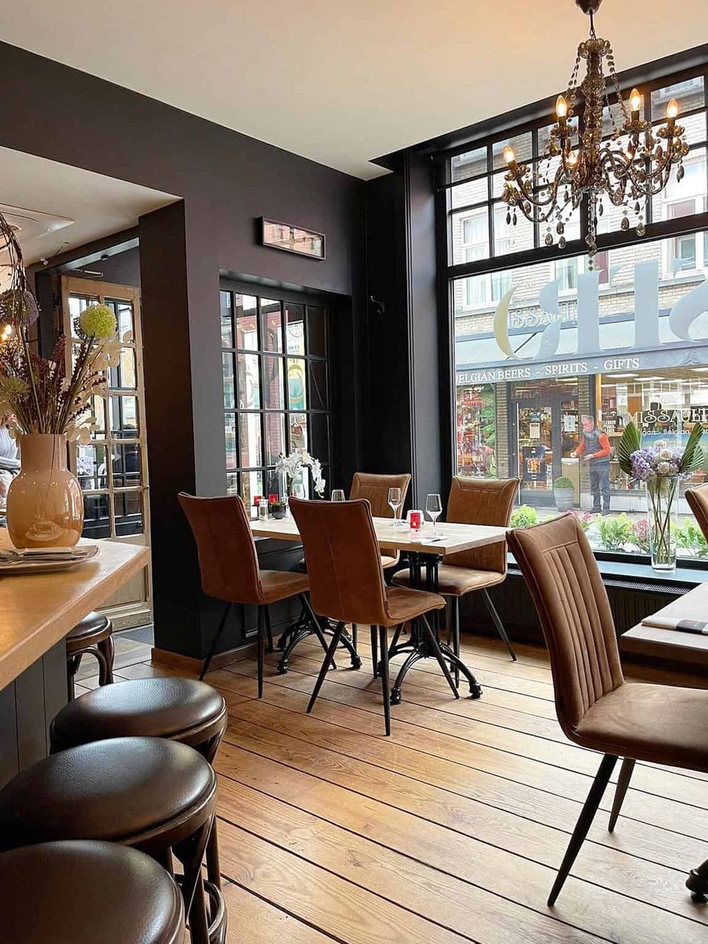 Stylish restaurant interior with large windows, elegant chandelier, and cozy seating for dining and drinks.