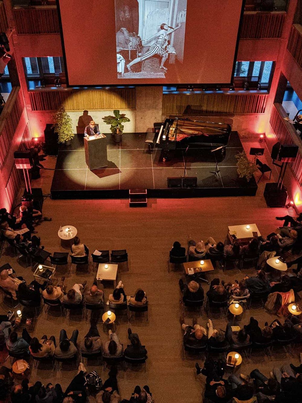 Elegant theater performance with a pianist, large screen, and an engaged audience, showcasing cultural events at QuestForDirections.