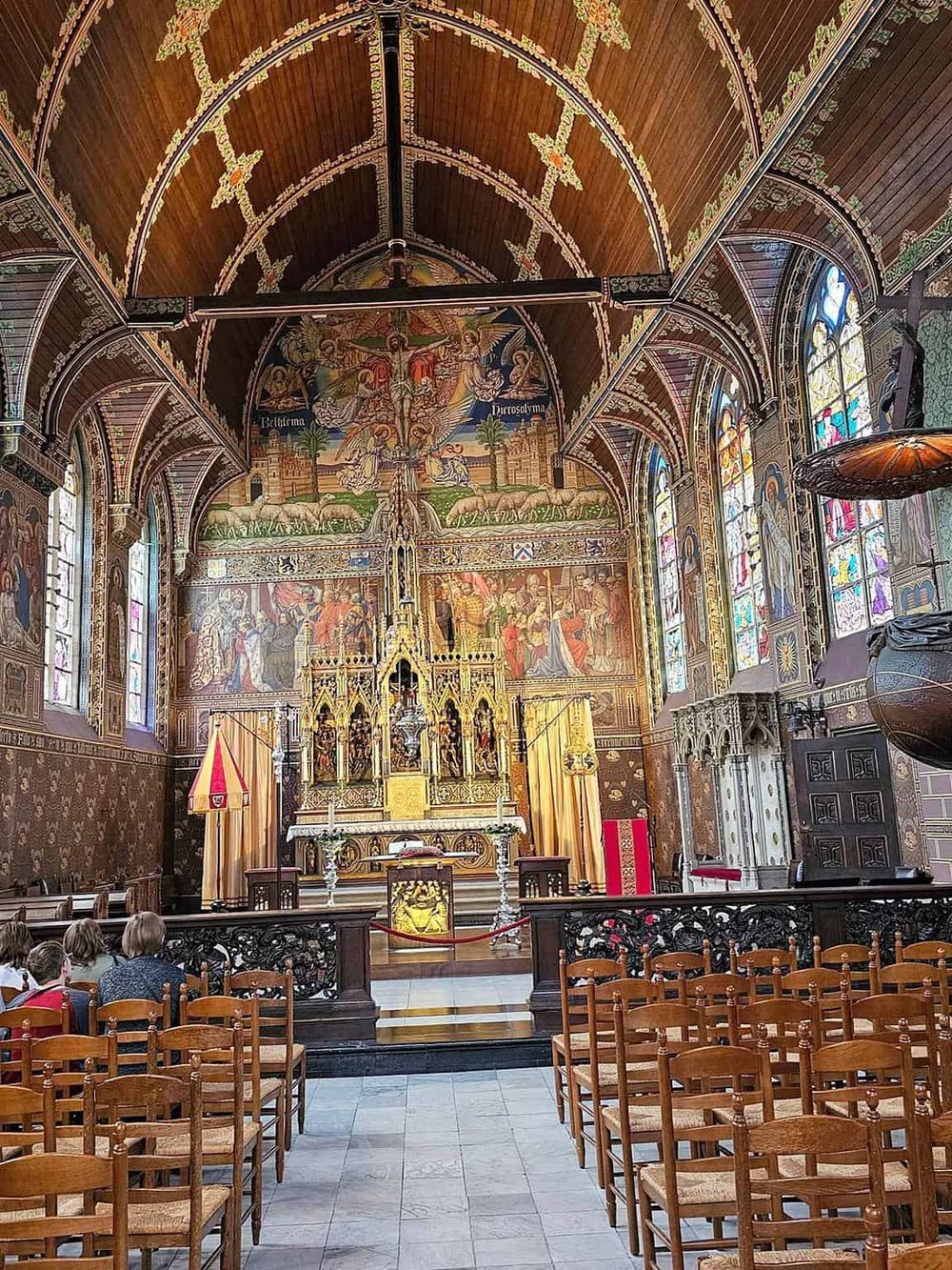 Vibrant church interior with ornate wooden ceiling, stained glass windows, and detailed religious murals.