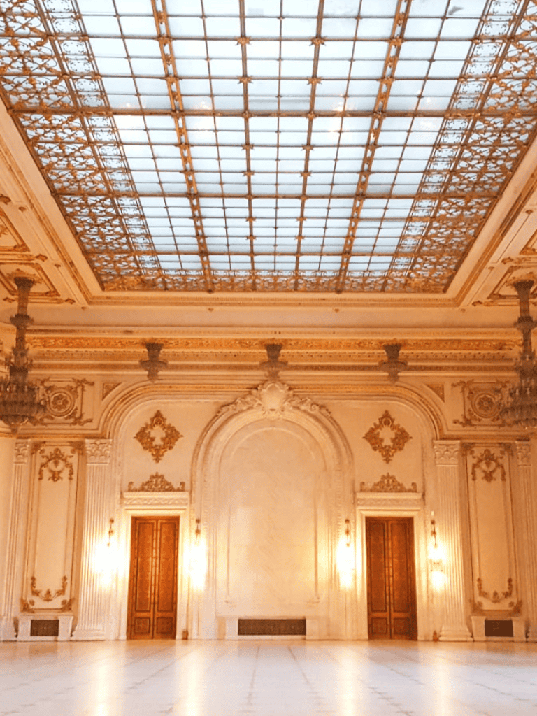 Elegant historic ballroom with ornate gold accents and a grand glass ceiling.