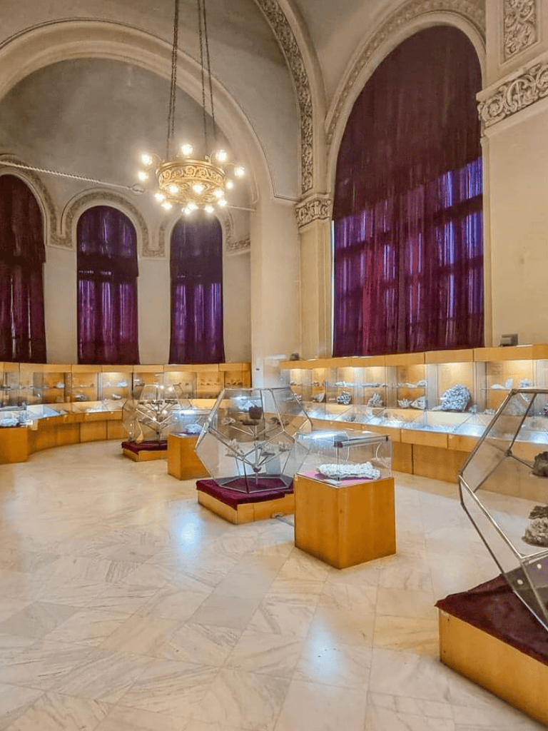 Intricate jewelry display in elegant museum setting with velvet curtains and ornate architecture.