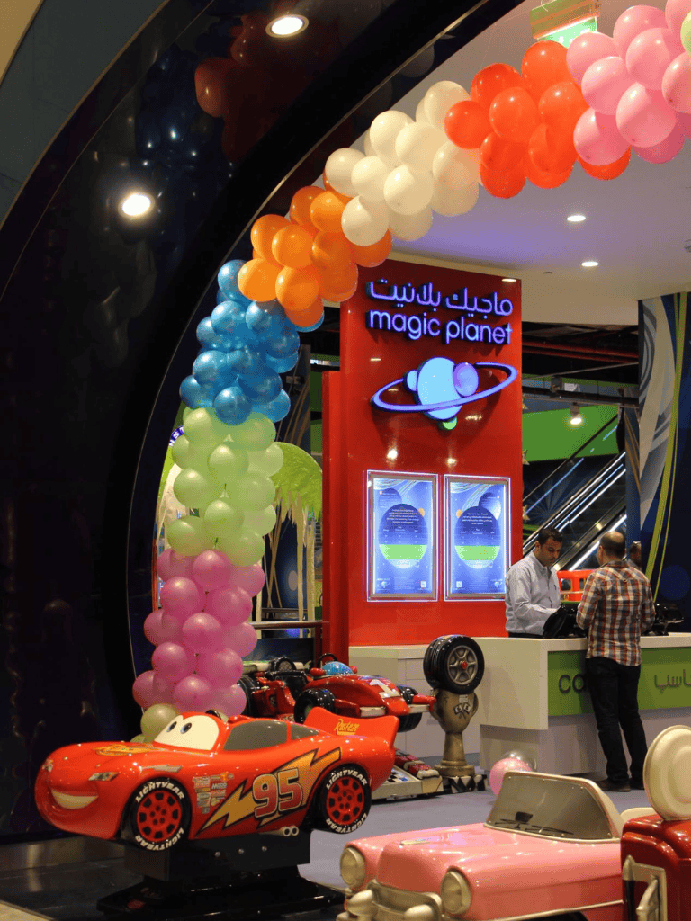 Brightly colored balloon arch at Magic Planet arcade with racing car rides for kids.