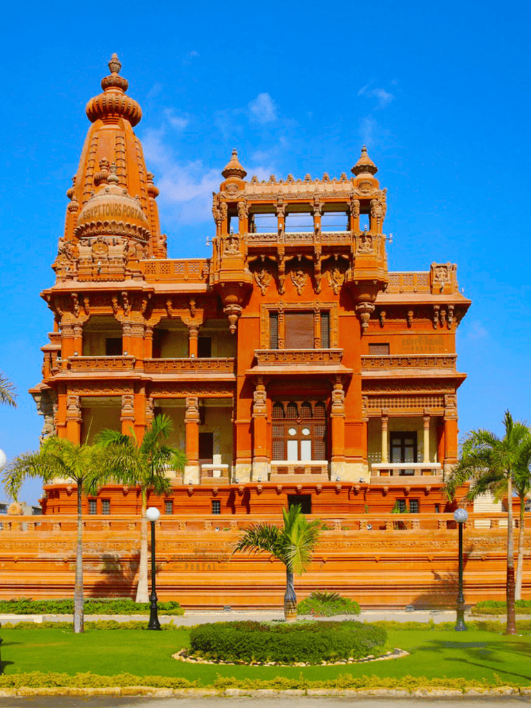 Ancient Indian temple architecture in warm sandstone with lush green landscaping and blue sky background.