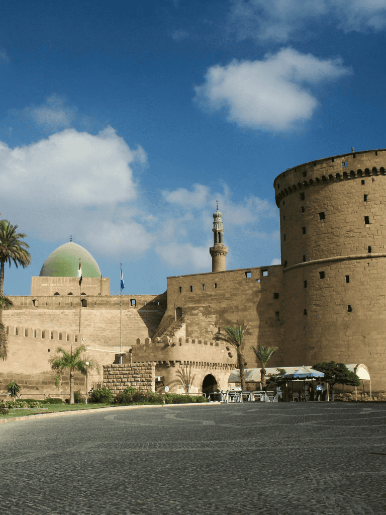 Ancient fortress and mosque in Aswan, Egypt with clear blue sky and palm trees.