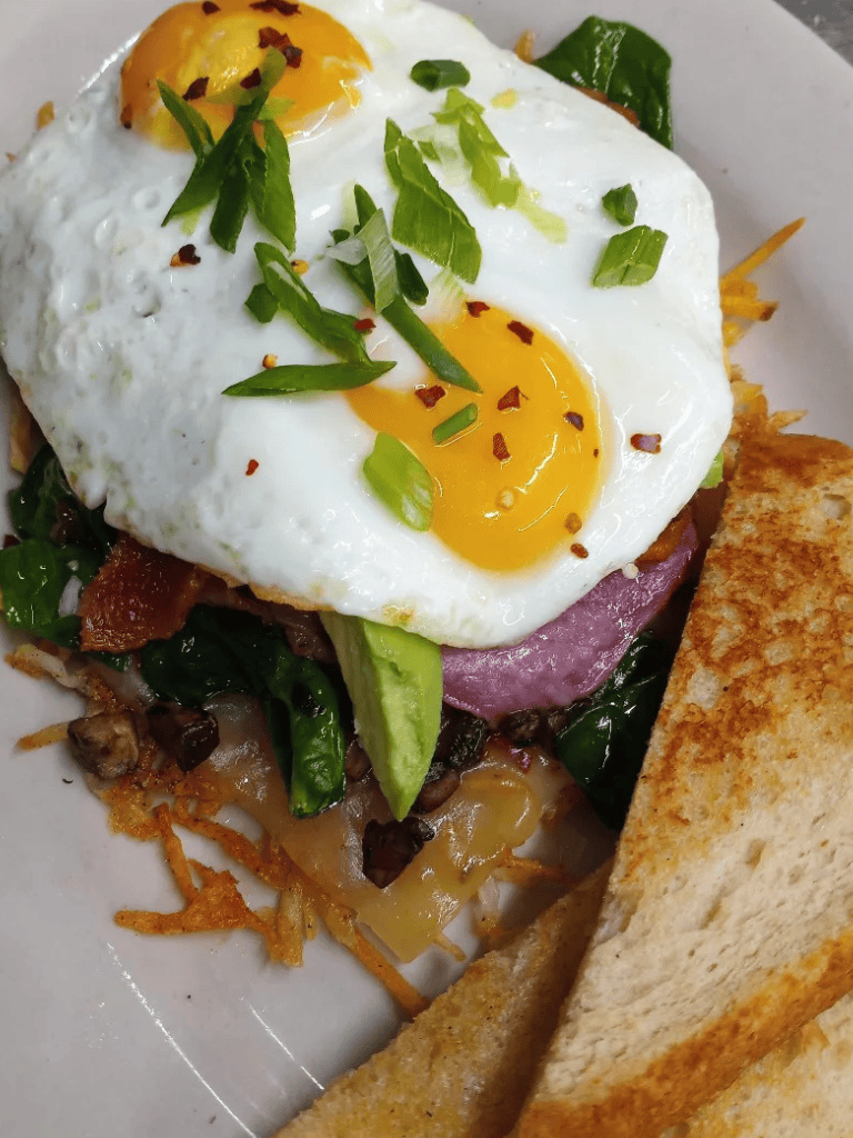 Fresh eggs with green onions and chili flakes on a breakfast sandwich with toast.