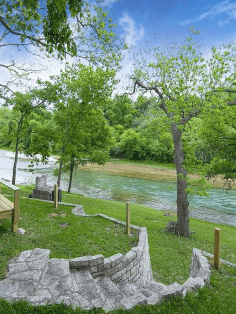 Tranquil riverside park with lush green trees and walking paths, perfect for outdoor relaxation and nature exploration.