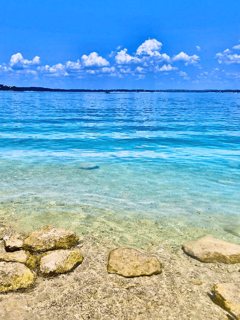 Crystal clear lake with rocky shoreline and blue skies, ideal for outdoor adventures and nature exploration.