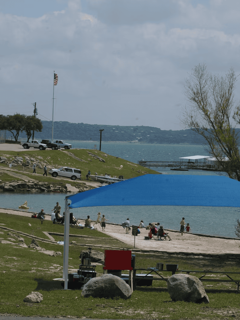 Flagpole with American flag, lakeside park, boating, and people enjoying outdoor recreation and scenic views.