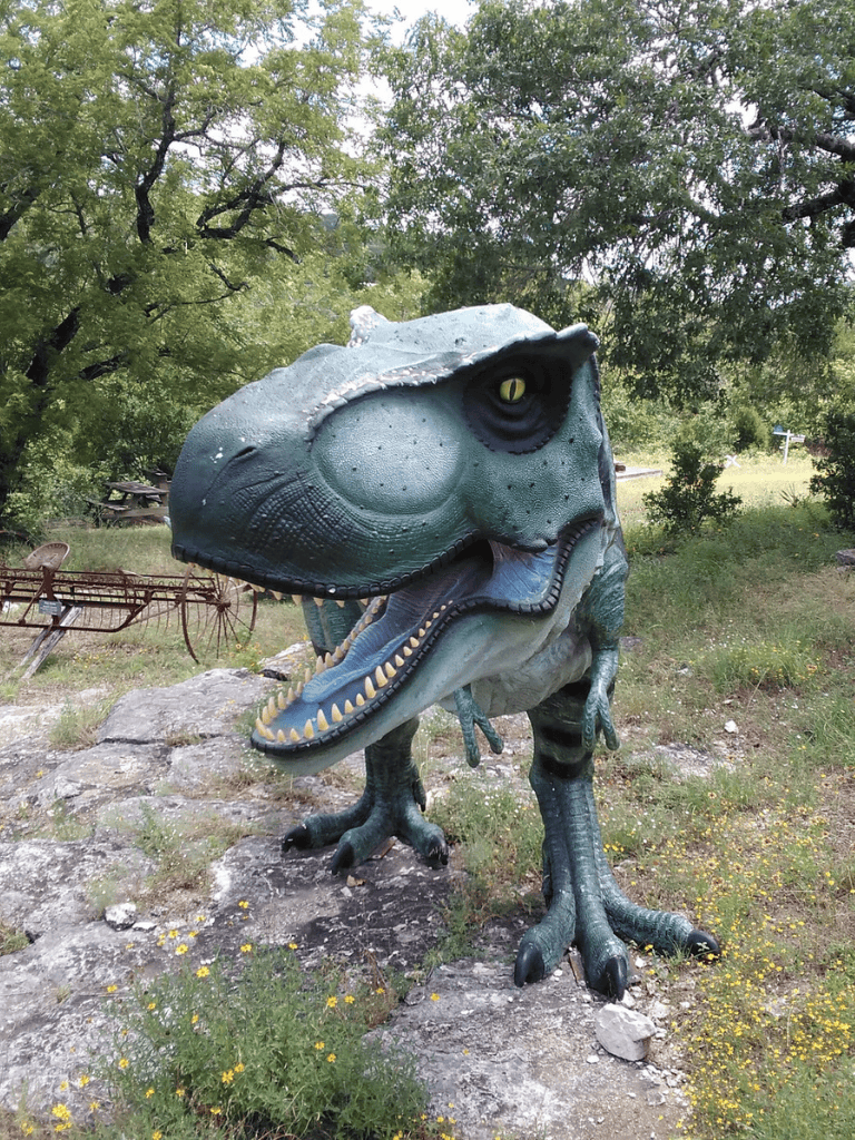 Large dinosaur sculpture outdoors in a natural setting at QuestForDirections.