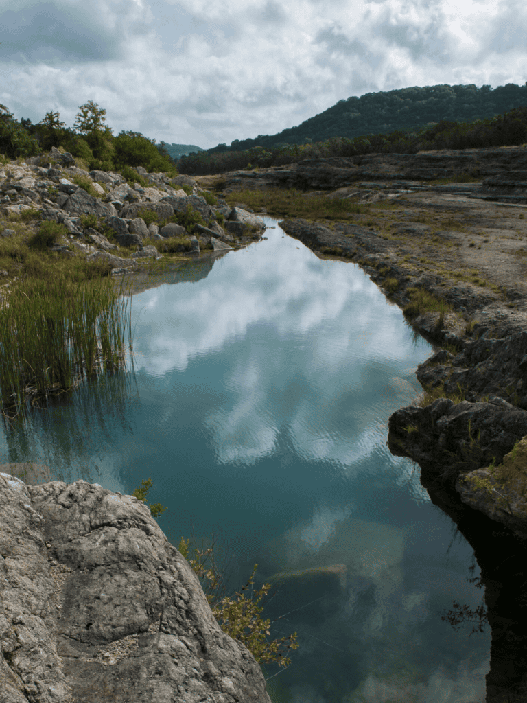 Tranquil river flowing through rocky landscape with distant mountains and cloudy sky.