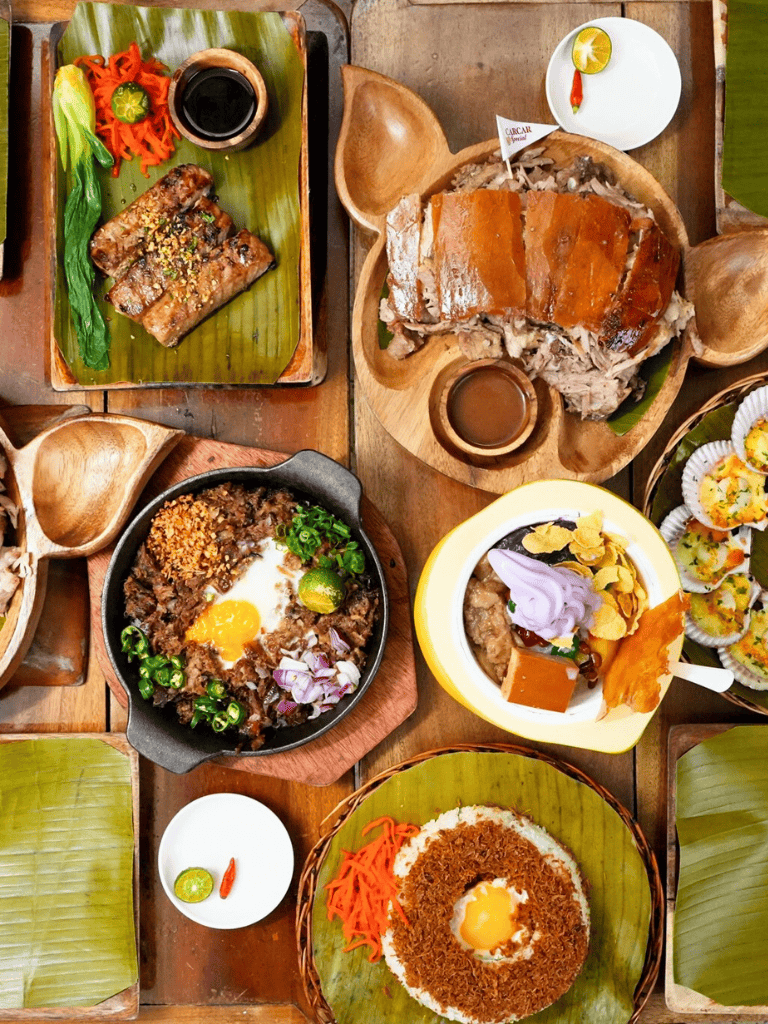 Tender roasted pork belly on traditional wooden platter with fresh vegetables, soy sauce, and chili.