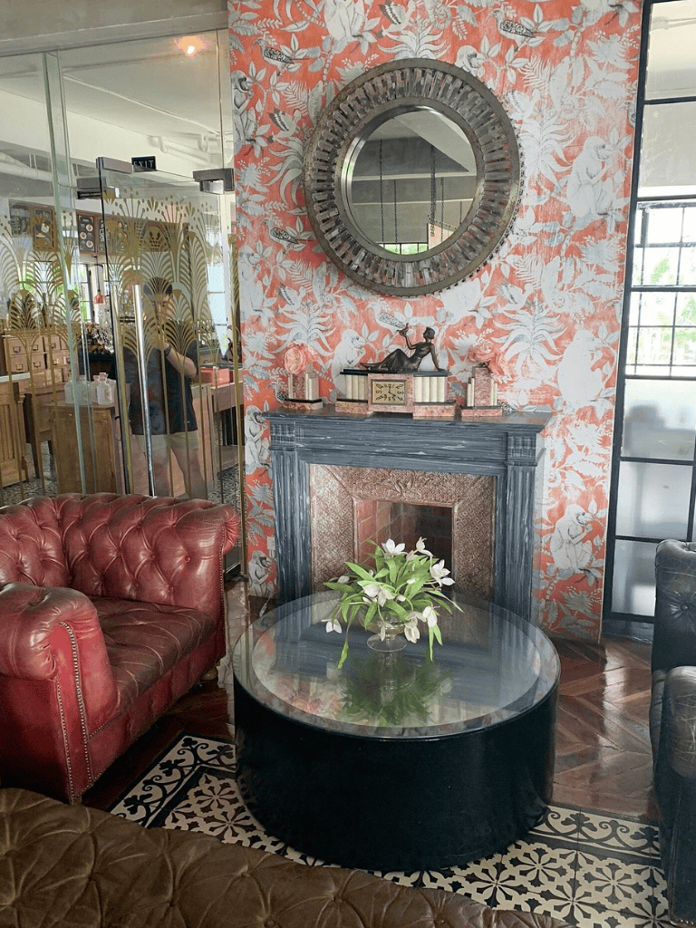 Cozy hotel lobby with marble fireplace, vintage decor, and floral wallpaper, inviting guests to relax.