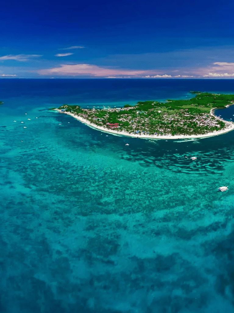 Aerial view of a tropical island with turquoise waters and boat cruises.