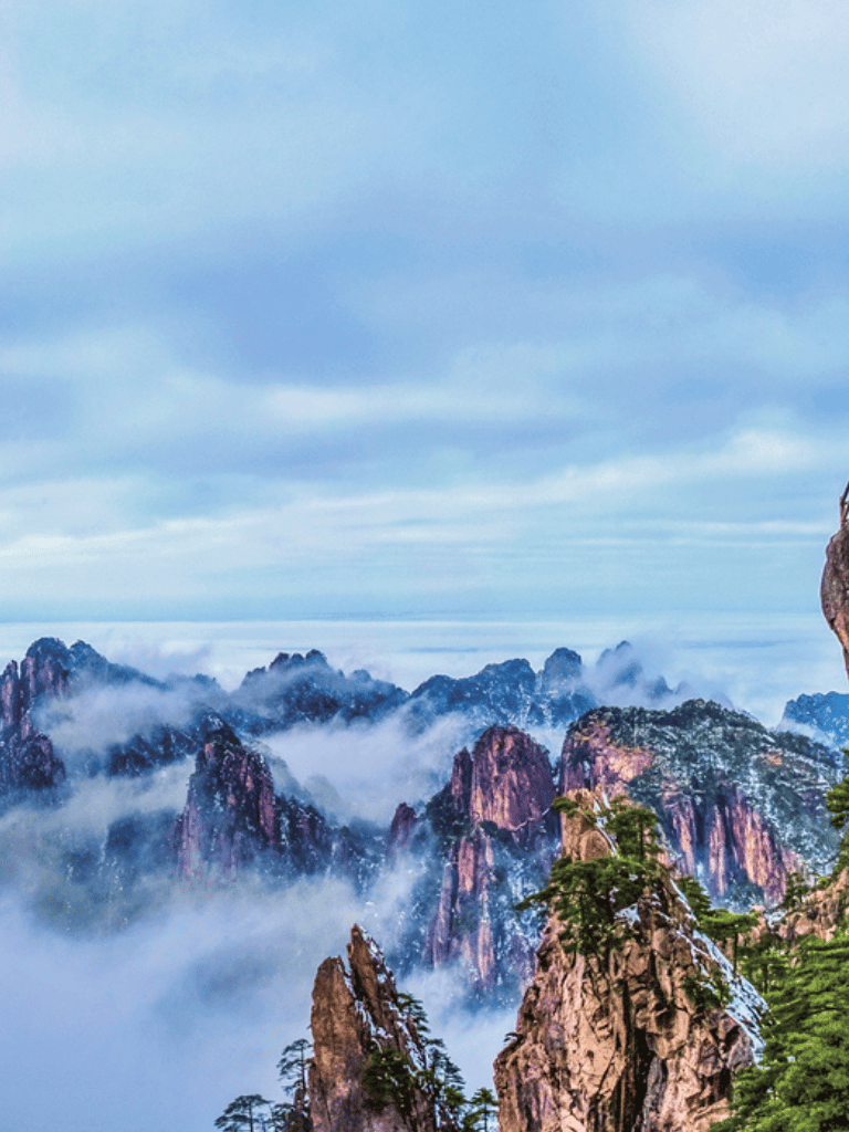 Stunning mountain landscape with misty clouds and lush trees on rocky peaks.