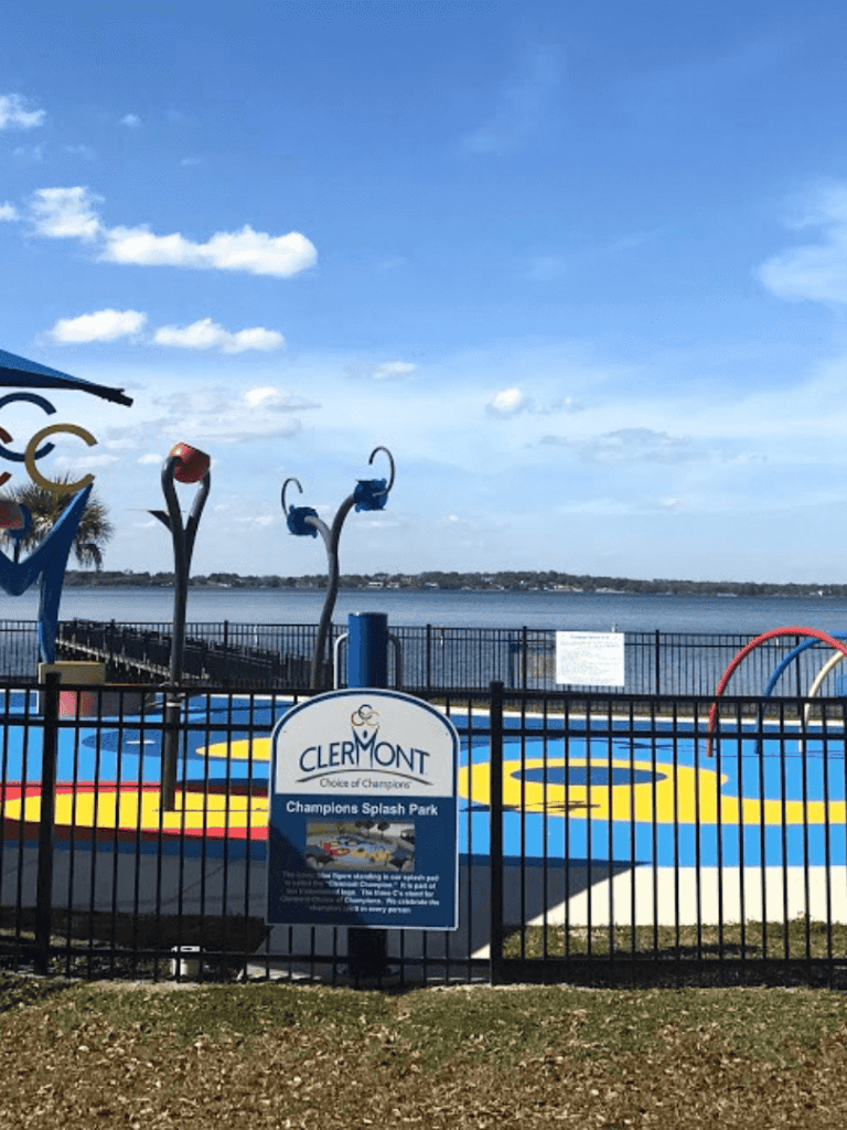Colorful splash pad at Clermont Champion Splash Park with water features and lake view, perfect for family fun.