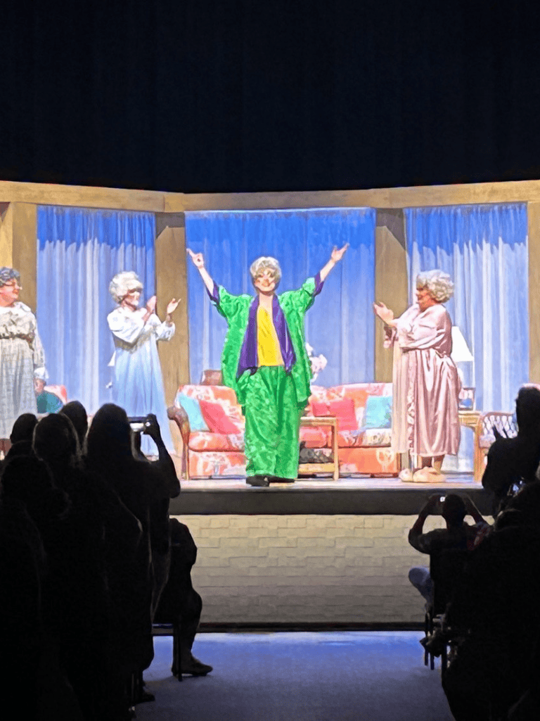 Older women performing on stage in a theatrical play with a living room set.