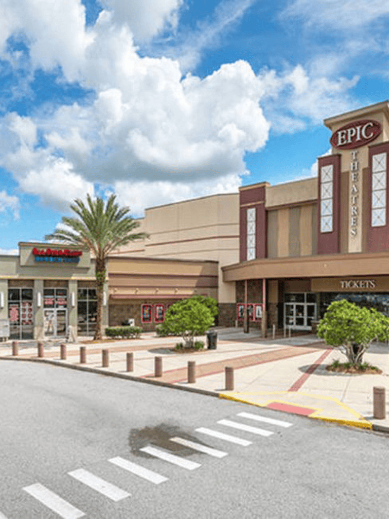 Bright shopping mall entrance with Epic Theatres, palm trees, and clear sky for easy directions.