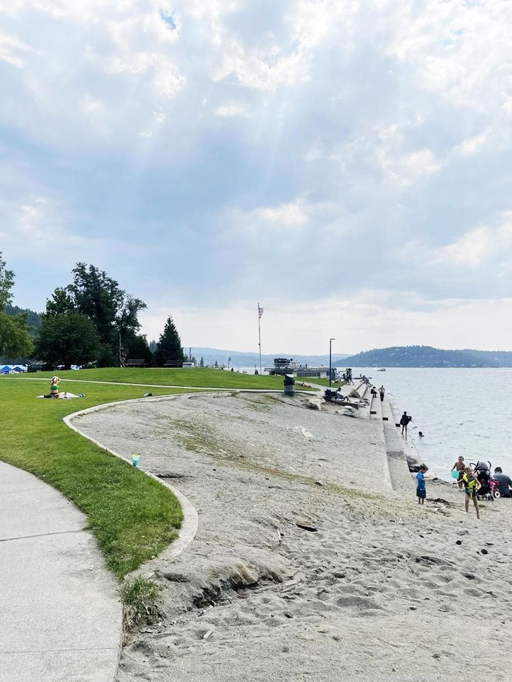 Serene lakeside park with walking paths, grassy areas, and people enjoying outdoor activities and scenic views.