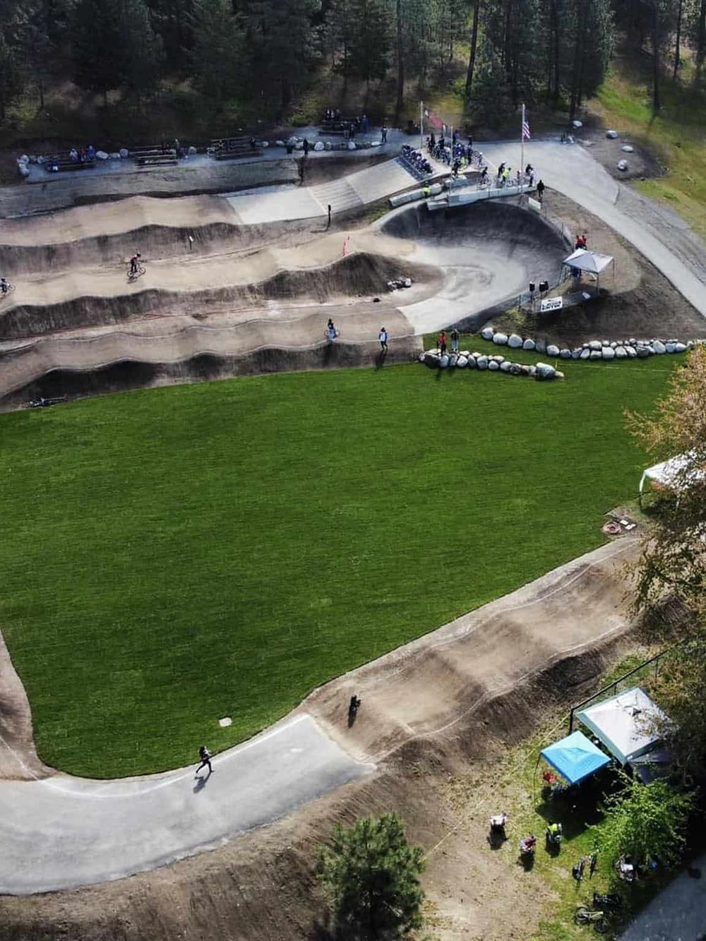Aerial view of a skatepark with dirt biking tracks, green grass, and spectators, showcasing outdoor recreational activities and bike trails.