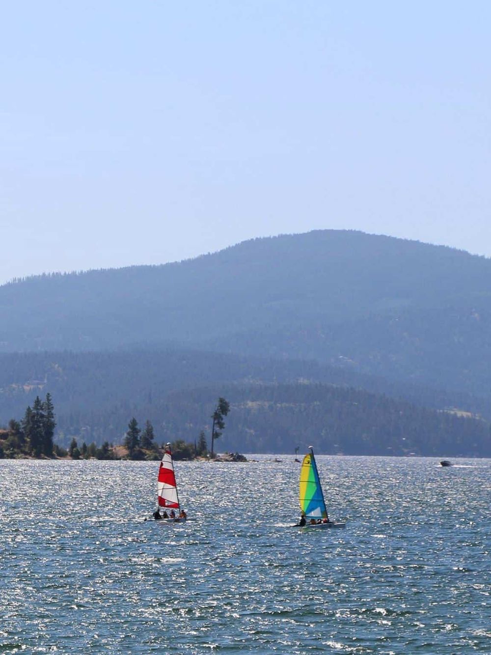 Colorful sailboats on a lake with scenic mountains in the background, ideal for outdoor adventure and navigation assistance.