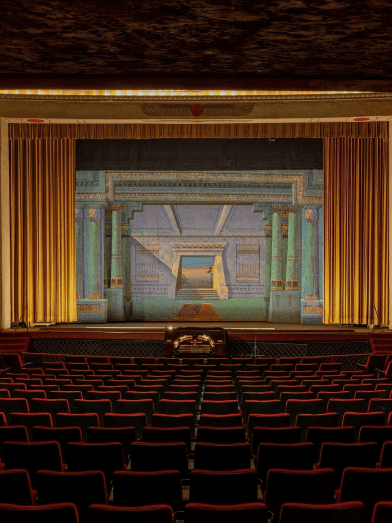 Vintage theater stage with ornate backdrop and red velvet seats for live performances and musicals.