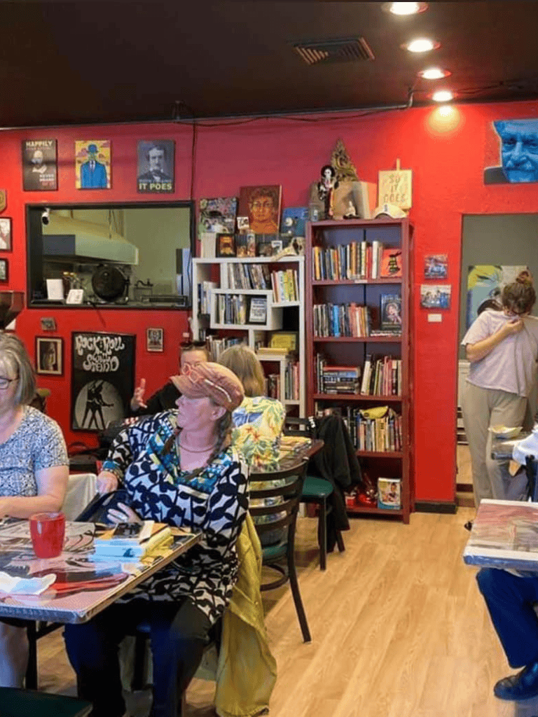 Cozy bookstore cafe with red walls, eclectic art, and shelves filled with books, hosting friendly readers and book lovers.