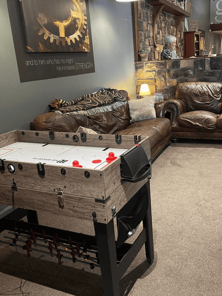 Cozy indoor lounge with foosball table, leather sofas, warm lighting, stone accent wall, and inspirational wall art.