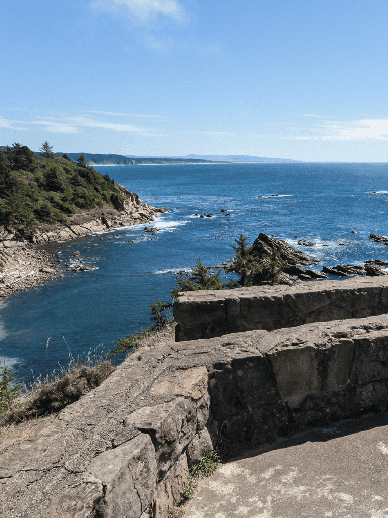 Breathtaking coastal view featuring rocky shoreline, ocean waves, and lush greenery under a clear blue sky.