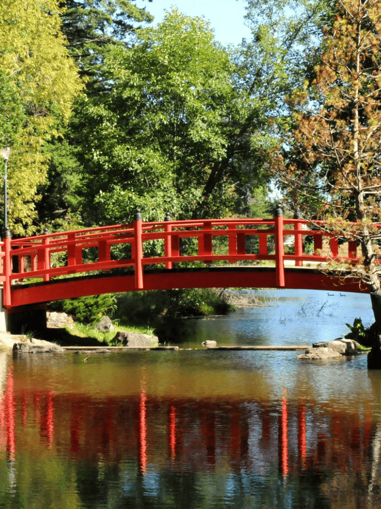 Decorative red bridge over a peaceful river surrounded by green trees.